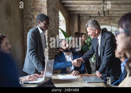 Caucasian and hispanic businessmen colleagues shaking hands on meeting in office, diverse entrepreneurs striking good deal, multiethnic teammates succ Stock Photo