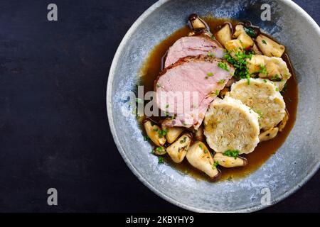 Traditional German pork roast served with bread dumpling and king oyster mushroom in dark beer sauce served as top view in a Nordic design bowl with c Stock Photo