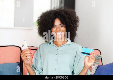 Excited multiracial female bank customer using phone to make easy secure payments online in convenient app. Glad black lady dream of spending bonus cashback received on credit card for internet paying Stock Photo