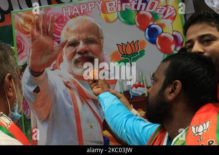 A supporter of India's Bharatiya Janata Party (BJP) symbolically holds a piece of Laddu ( Sweet) next to the portrait of Indian Prime Minister Narendra Modi during Modi's 70th birthday celebrations, in Kolkata, India, on September 17, 2020. (Photo by Debajyoti Chakraborty/NurPhoto) Stock Photo