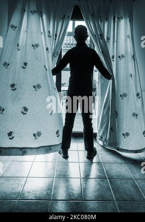 Rear view of man looking through patio window Stock Photo