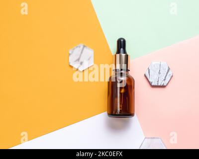Top view on glass bottles of essential oil or cosmetic serum on colorful geometrical background. Decorative marble and glass hexagons. Stock Photo