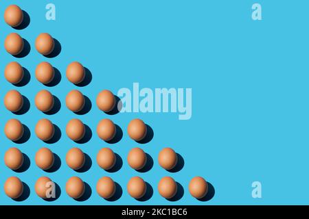 A pattern of brown chicken eggs lying diagonally on the left half of the blue background. Right side for copy space, close-up, top view. Stock Photo