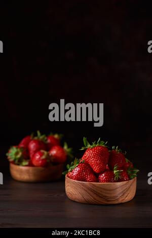 Fresh red strawberries in two wooden bowls on a brown wooden table. Vertical, copy space, close-up. Stock Photo