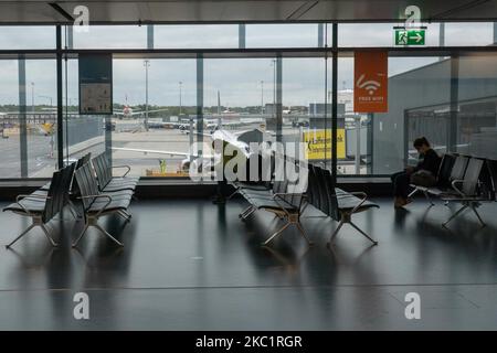 Passengers with facemask sitting infront of the window with aircraft in the background. Passengers wearing facemasks, face shields, gloves and other safety measures are seen in the airport terminal, at the F Gates area of Vienna International Airport VIE LOWW - Flughafen Wien-Schwechat serving the Austrian Capital but also Bratislava as it is 55km away from the Slovak city during the Covid-19 Coronavirus pandemic era. There is a second wave coming while cases are increasing, facemask become mandatory, social distancing measures and disinfecting hand sanitizer are everywhere while new lockdowns Stock Photo