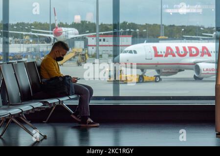 Passengers with facemask sitting infront of the window with aircraft in the background. Passengers wearing facemasks, face shields, gloves and other safety measures are seen in the airport terminal, at the F Gates area of Vienna International Airport VIE LOWW - Flughafen Wien-Schwechat serving the Austrian Capital but also Bratislava as it is 55km away from the Slovak city during the Covid-19 Coronavirus pandemic era. There is a second wave coming while cases are increasing, facemask become mandatory, social distancing measures and disinfecting hand sanitizer are everywhere while new lockdowns Stock Photo