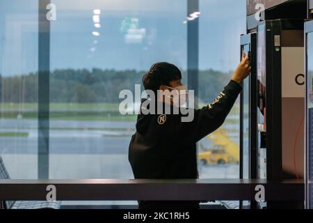 Asian passengers is using the vending machine at the airport while he wears a facemask. Passengers wearing facemasks, face shields, gloves and other safety measures are seen in the airport terminal, at the F Gates area of Vienna International Airport VIE LOWW - Flughafen Wien-Schwechat serving the Austrian Capital but also Bratislava as it is 55km away from the Slovak city during the Covid-19 Coronavirus pandemic era. There is a second wave coming while cases are increasing, facemask become mandatory, social distancing measures and disinfecting hand sanitizer are everywhere while new lockdowns Stock Photo