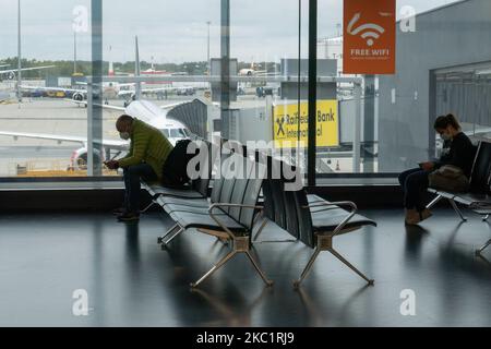 Passengers with facemask sitting infront of the window with aircraft in the background. Passengers wearing facemasks, face shields, gloves and other safety measures are seen in the airport terminal, at the F Gates area of Vienna International Airport VIE LOWW - Flughafen Wien-Schwechat serving the Austrian Capital but also Bratislava as it is 55km away from the Slovak city during the Covid-19 Coronavirus pandemic era. There is a second wave coming while cases are increasing, facemask become mandatory, social distancing measures and disinfecting hand sanitizer are everywhere while new lockdowns Stock Photo