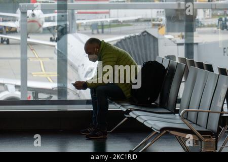 Passengers with facemask sitting infront of the window with aircraft in the background. Passengers wearing facemasks, face shields, gloves and other safety measures are seen in the airport terminal, at the F Gates area of Vienna International Airport VIE LOWW - Flughafen Wien-Schwechat serving the Austrian Capital but also Bratislava as it is 55km away from the Slovak city during the Covid-19 Coronavirus pandemic era. There is a second wave coming while cases are increasing, facemask become mandatory, social distancing measures and disinfecting hand sanitizer are everywhere while new lockdowns Stock Photo