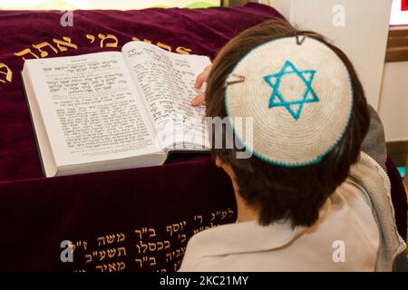 A rear view of praying young man pointing at a phrase in a bible book (sefer torah), while reading a pray Stock Photo