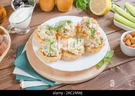 Tartlets stuffed with Olivier salad on a white plate on a dark wooden background. Stock Photo