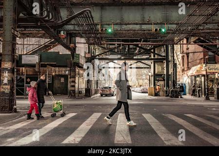 A man passing a cross road with two children behind. Daily life view of the road and street under the subway railroad air-bridge metal construction of M, J and Z lines near Marcy Ave station, with restaurants, shops, the famous dollar slice pizza, traffic with cars and trucks and with sidewalks in Broadway street in Brooklyn, New York City. Brooklyn is the most populous county in the state of New York and the second-most densely populated in the United States. Brooklyn, NY, USA on 13 February 2020. (Photo by Nicolas Economou/NurPhoto) Stock Photo