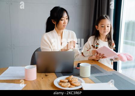 Asian girl doing homework with her mother in kitchen at home Stock Photo