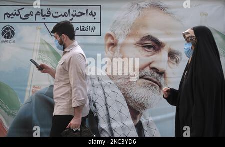 An Iranian man and a veiled woman wearing protective face masks walk past a portrait of the former commander of Iran’s Islamic Revolutionary Guards Corps (IRGC) Quds Force, Ghasem Soleimani, in the holy city of Mashhad in Razavi Khorasan province 891Km (554 miles) east of Tehran on November 10, 2020, Amid the new coronavirus disease (COVID-19) outbreak in Iran. After Iranian Governments re-announced red alarm in the Iranian holy city of Mashhad and the capital of Khorasan Razavi province, the use of masks in public places became mandatory. (Photo by Morteza Nikoubazl/NurPhoto) Stock Photo