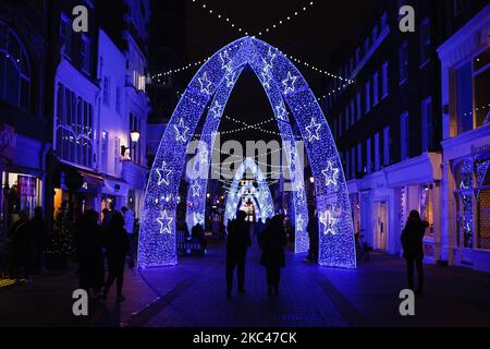 People walk under Christmas lights on South Molton Street in London, England, on November 18, 2020. Across England non-essential shops as well as bars, restaurants and other hospitality businesses remain closed as part of the country's second national coronavirus lockdown, begun on November 5 and set to expire on December 2. British Prime Minister Boris Johnson, who has indicated that he does not wish for the lockdown to be extended, meanwhile remains in self-isolation at Downing Street after coming into contact with an MP last Thursday who later tested positive for covid-19. The prime ministe Stock Photo