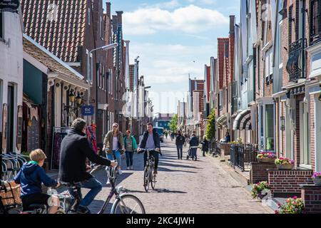 People strolling or riding a bicycle in Volendam. Daily life in Volendam traditional fishing village with Dutch architecture in North Holland near Amsterdam in The Netherlands. Volendam has a harbor and is a popular destination and tourist attraction in the country. There are old fishing boats, traditional clothing of locals, ferry ride to Marken, museums, cheese factroy, cafe and souvenir shops at the waterfront and a little beach. There are houses along the shore and a marina nearby for tourists and locals as visitors so tourism is the main income for the community. Volendam has been feature Stock Photo