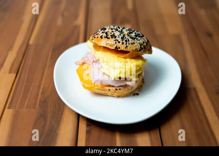 A closeup of a cheeseburger with fried eggs and ham on a white plate Stock Photo