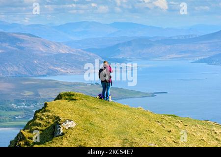 A walker on the summit ridge of Ben Tianavaig admiring the view over the Inner Sound towards the mainland.  Near Portree, Isle of Skye, Scotland, UK Stock Photo