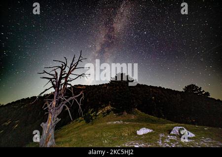 Milky Way captured with long exposure photography technique. Milkyway is the visible part of our galaxy that contains our Solar System as seen during the night from Olympus Mountain the mythical mountain in Ancient Greek culture, between Petrostrouga refuge and Skourta peak at the hiking trail above 2000m above the sea level in Greece during the night. Night landscape with trees, forest, summits with colorful Milky Way sky dome, cloudless sky at mountains with the starry sky with hills at summer with the beautiful Universe and Space background. Olympus Mountain National Park, Greece - October  Stock Photo