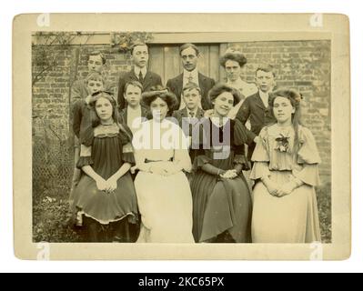 Original Edwardian cabinet card of teenage boys and girls, friends, outside in the garden, perhaps a coming of age photograph for the girl in the white dress with her hair in an adult hairstyle, younger ones are wearing their hair loose. Circa 1906 U.K. Stock Photo