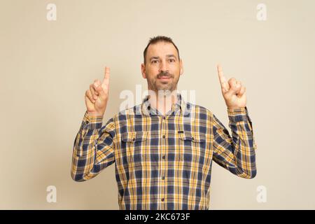 Portrait of a happy bearded man pointing fingers at copyspace isolated over beige background. Stock Photo