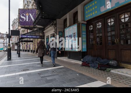 A couple walks past a homeless person seeking shelter in a doorway of a closed theatre in the West End as tier 4 coronavirus restrictions are in place to limit the spread of the new strain of coronavirus as the infections continue to rise, on 22 December, 2020 in London, England. London, the south-east and the east of England entered tier 4 restrictions on Sunday, similar to the last national lockdown, with an order to stay-at-home, ban on household mixing, closing of all non-essential retail and businesses and cancellation of the planned relaxing of rules over five days around Christmas. (Pho Stock Photo