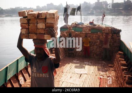 Laborers unload bricks from a cargo ship at Kamrangirchar area in Dhaka ...