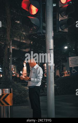 An Asian man in formal clothes looking at his phone and listening to music at the red light Stock Photo