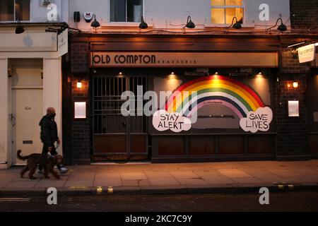 A man wearing a face mask walks a dog past a rainbow mural calling for people to 'Stay Alert, Save Lives', painted onto the boarding of a temporarily-closed brasserie on a near-deserted Old Compton Street in the Soho district of London, England, on January 12, 2021. England began the second full week of its third national coronavirus lockdown today, imposed by British Prime Minister Boris Johnson following health authorities' warnings that the National Health Service (NHS) could soon be overwhelmed with patients with covid-19. (Photo by David Cliff/NurPhoto) Stock Photo