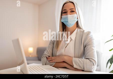 Pensive female entrepreneur with face mask working on business reports in the office. Stock Photo