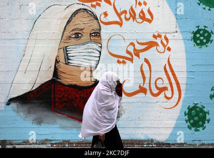 A Palestinian woman walks past graffiti with a slogan in Arabic reading: 'protect yourself and your family', amid the Covid-19 pandemic in Gaza City on January 13, 2021. (Photo by Majdi Fathi/NurPhoto) Stock Photo