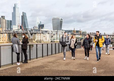 Passers-by are seen walking on Sunday sunny afternoon in Southbank embankment by the Thames River with the City in the background as the UK's government introduced strict Coronavirus restrictions earlier this month due to sharp increase in numbers of Covid-19 cases in the UK - London, England on January 17, 2021. Under the new regulations people are only allowed to take short walks locally within their limited social bubble as an exception for Stay at Home policy., 2021. Under the new regulations people are only allowed to take short walks locally within their limited social bubble as an excep Stock Photo