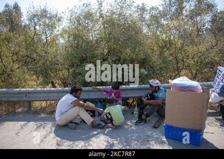 A family is having lunch roadside after getting some food from a humanitarian organization. Humanitarian Aid is given to Asylum Seekers from Team Humanity Denmark NGO after the refugees and migrants have their body temperature tested, in order to prevent people to enter the facility with the possibility of spreading the pandemic, the Covid-19 Coronavirus. The facility is near the former Moria hotspot camp. More than 10.000 Asylum Seekers are homeless and helpless, resulting sleeping and living roadside without any shelter, food, running water supply, facility, infrastructure or help after the  Stock Photo