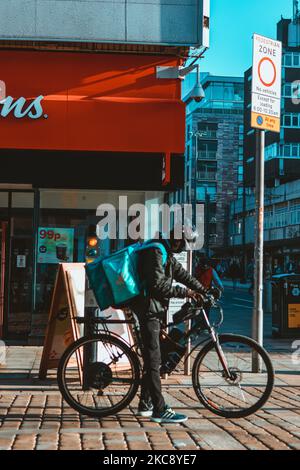 A delivery man riding a bicycle on the street of Manchester City Centre, UK Stock Photo