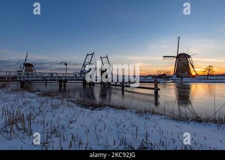 Magical scnery around the sunset time and dusk with clear winter sky at the frozen canals and Windmills of Kinderdijk in the Netherlands. The country is facing arctic weather, severe low temperatures, snowfall and high winds due to storm Darcy that caused problems in transportation and every day life. Many of the canals have been ice frozen as there is subzero temperature from the cold weather sometimes reaching -16C, while the land is covered by snow. Kinderdijk and the Windmills in the Alblasserwaard polder, is a famous attraction, a Dutch landmark and a UNESCO World Heritage Site, attractin Stock Photo