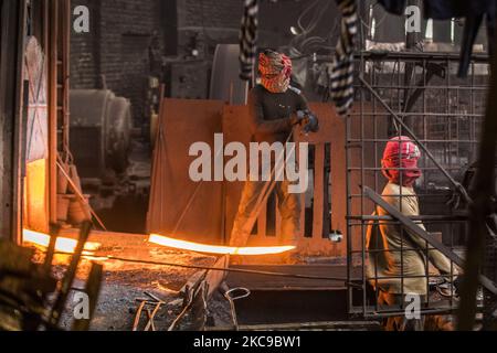 Bangladeshi rolling mill worker seen working in the steel re-rolling mill without proper safety gear or tools in Postagola, Bangladesh on February 15, 2021. In these mills iron is forged in 1200 + to 1300+ Celsius. In such a heated place the soles of their shoes are likely to be burnt off with one careless step. (Photo by Ahmed Salahuddin/NurPhoto) Stock Photo