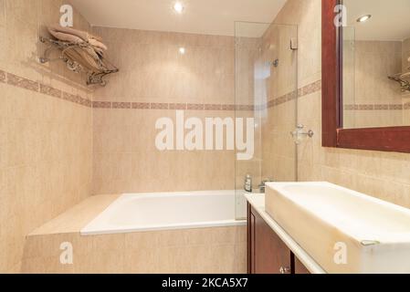 bathroom with white stone vanity and sink with matching mahogany mirror, walk-in tub and cream tile Stock Photo