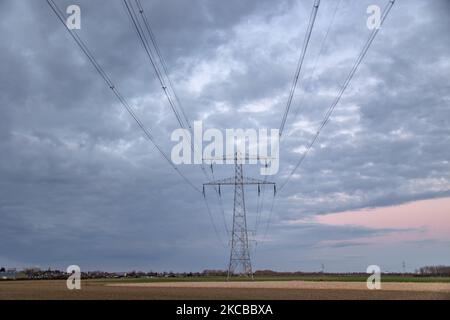 High voltage electricity poles during magic hour. The metal towers as seen in the sunset in the Dutch countryside distribute electric energy from the power station, Belgium and Germany across the country. The electric wires, the grid and pillars or power pylons are seen as silhouettes in the colorful cloudy dusk sky. Stevensweert, the Netherlands on March 19, 2021 (Photo by Nicolas Economou/NurPhoto) Stock Photo