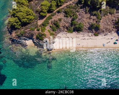 Aerial bird's eye panoramic view from a drone of Aretes beach, in Toroni area, a hidden gem in Halkidiki. The beach with the golden sand and transparent crystal-clear emerald water, exotic and tropical style with pine trees near the sand, typical for the Aegean Sea and the Mediterranean consists of 3 different bays as seen with some tourists who arrived by a little ship. The coastline protected by rocky hills around is a hidden treasure for locals and tourists without the overcrowded summer scenes with the beach bars. Chalkidiki is a popular holiday destination, famous for the best beaches in  Stock Photo