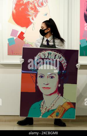 An art handler poses holding 'Queen Elizabeth II, from: Reigning Queens', by American artist Andy Warhol, estimated at GBP70,000-100,000, and in front of one of Warhol's set of four 'Queen Margarethe II of Denmark, from: Reigning Queens (Royal Edition)', estimated at GBP60,000-80,000, during a press preview at Christie's auction house in London, England, on March 26, 2021. (Photo by David Cliff/NurPhoto) Stock Photo