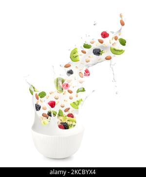 Bowl with splashing milk, sweet oatmeal, falling fruits and nuts on white background Stock Photo
