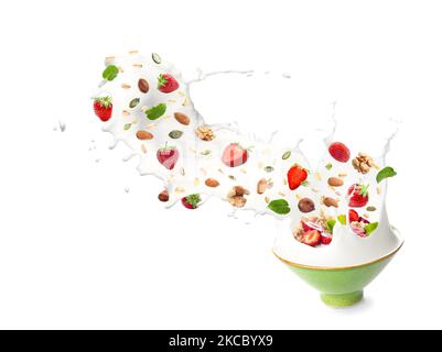 Bowl with splashing milk, sweet oatmeal, falling strawberries and nuts on white background Stock Photo