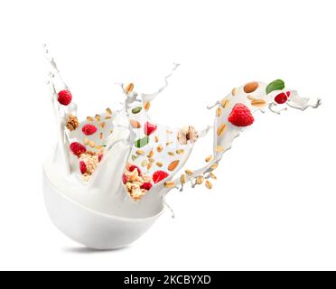 Bowl with splashing milk, sweet oatmeal, falling raspberries and nuts on white background Stock Photo