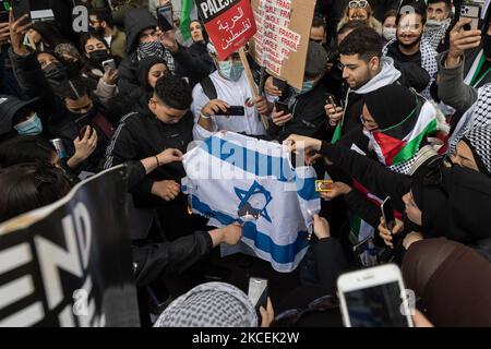 LONDON, UNITED KINGDOM - MAY 15, 2021: Demonstrators burn the Israeli flag as thousands of people gather outside the Israeli Embassy after marching from Hyde Park in central London to protest against air strikes on Gaza, on 15 May, 2021 in London, England. Conflict between Israel and Palestine has escalated in recent weeks fueled by the planned evictions of Palestinian families from their homes by Jewish settlers in the Sheikh Jarrah district of East Jerusalem and clashes with security forces around the Old City during Ramadan, leading to exchange of air strikes by Hamas and the Israeli milita Stock Photo