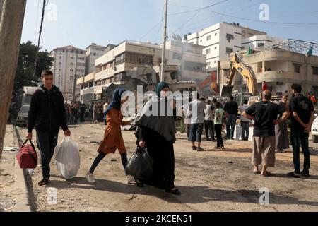 Palestinian families walk past destroyed buildings as they leave their homes in Gaza City with some belongings to shelter in a safer neighbourhood, following massive Israeli bombardment early on May 16, 2021. - The previous day, an Israeli air strike flattened a 13-floor building housing Qatar-based Al Jazeera television and the US news agency the Associated Press in the Gaza Strip. (Photo by Majdi Fathi/NurPhoto) Stock Photo