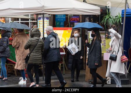 LONDON, UNITED KINGDOM - MAY 17, 2021: A waiter stands with a menu outside a restaurant in Chinatown while pedestrians shetlter from the rain as England moves to Step 3 in easing of coronavirus restrictions, on 17 May, 2021 in London, England. From today indoor hospitality and entertainment venues are allowed to re-open, six people or two households can meet indoors and international travel without need for quarantine resumes to 12 green list countries, however there are concerns that the surge in cases of the Indian Covid variant may delay the fourth stage of easing lockdown on June 21. (Phot
