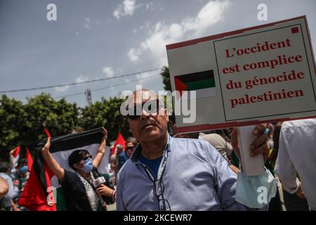 A protester lifts a placard that reads in French, the West is complicit in the Palestinian genocide, during a demonstration held in front of the Tunisia's parliament's building in the city of Bardo Tunis, Tunisia, on May 18, 2021, to call for the adoption of a law by the parliament, that criminalizes all forms of normalization of relations with Israel. Demonstrators also protested against the Israeli air strikes on Gaza Strip as well as the Israeli violations in the occupied territories in Palestine, especially in the Palestinian neighbourhood Sheikh Jarrah in East Jerusalem. The protest comes Stock Photo