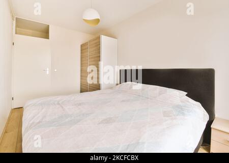 Comfortable bed with ornamental blanket placed near glass door and wardrobe with mirror in light bedroom Stock Photo