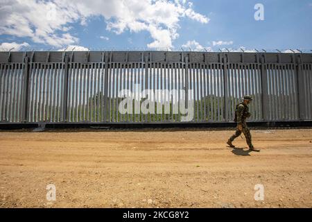 An armed military personnel is patroling along the fence, while there is a Turkish watchtower in the background behind the new fence. Greece is reinforcing the Greek Turkish borders with personnel, cameras, drones, heavy vehicles, FRONTEX officers but also with a 5 meter tall fence. The fence is actually a concrete filled, a construction for at least 40KM, a long coverage in the wetlands of Evros river (Meric in Turkish), Greece's river border with Turkey. EU is supporting the border fortification financially. Asylum seekers, migrants and refugees used Evros as an entrance point to Europe, whi Stock Photo