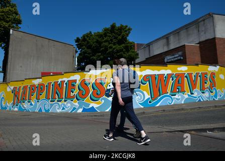 A couple walks past a new mural 'Happiness Waves' in Dún Laoghaire city center. From June 22nd, Dún Laoghaire’s streets and lane-ways getting brightened by a host of street artworks as part of the Dún Laoghaire Anseo project. On Sunday, 27 June 2021, in Dublin, Ireland. (Photo by Artur Widak/NurPhoto) Stock Photo